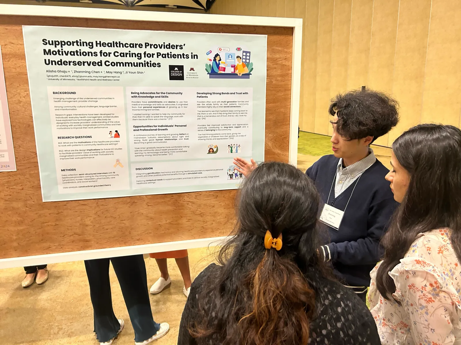 Zhanming Chen points at the poster while two attendees, seen from behind, read it.
