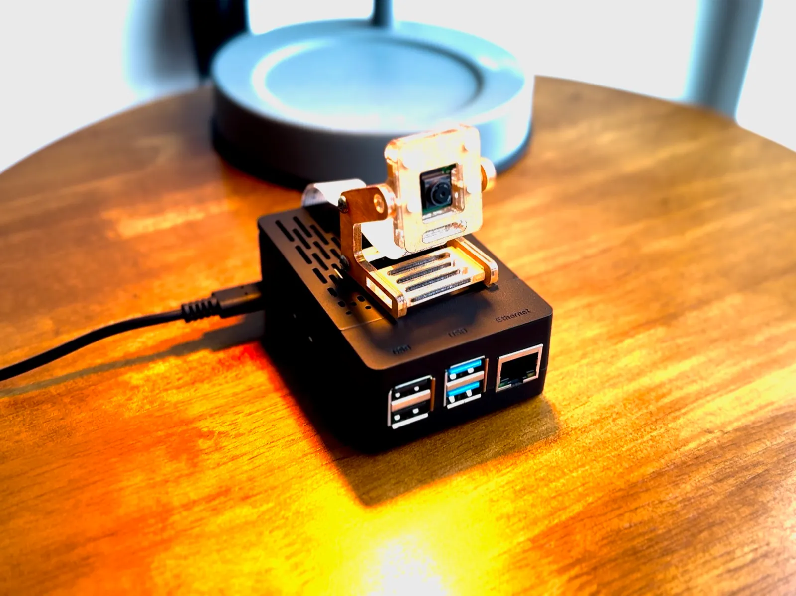 The Raspberry Pi in its closed black case, camera module mounted on a clear stand on top
