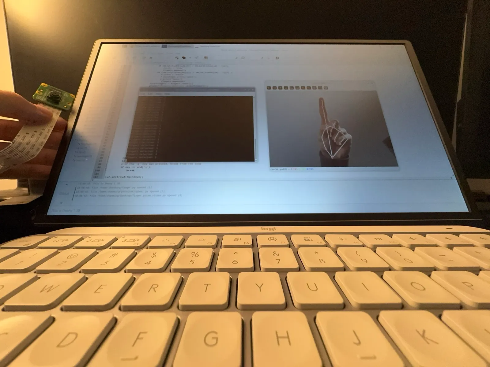 Monitor showing code, a terminal printing finger counts, and a camera view of a raised finger with landmarks